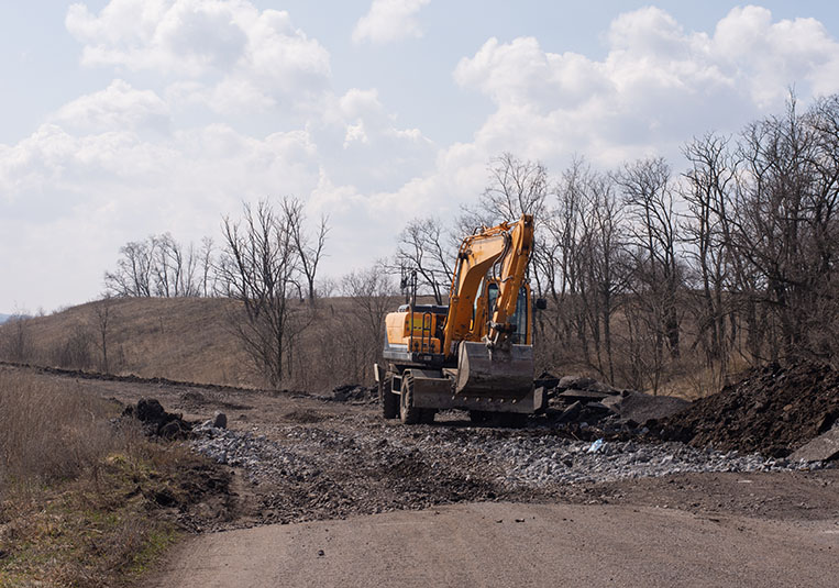 A large construction vehicle parked on a dirt road, surrounded by a construction site and scattered debris.